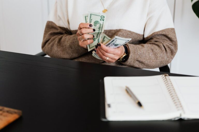Close-up of an adult counting dollar bills at a desk with a notebook.